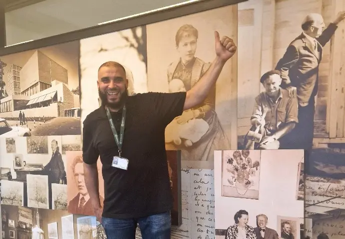 Hicham staat trots bij de kunstwerken van het Van Gogh Museum, waar hij als objectleider bij Breedweer de facilitaire dienstverlening verricht